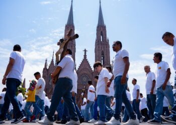 Caminata de devotos durante la Procesión del Silencio en Michoacán, con la majestuosa catedral de fondo en un día soleado.