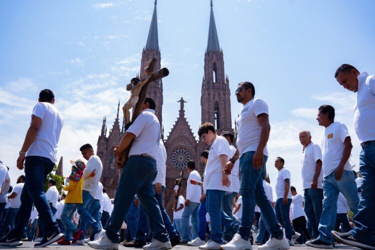 Caminata de devotos durante la Procesión del Silencio en Michoacán, con la majestuosa catedral de fondo en un día soleado.