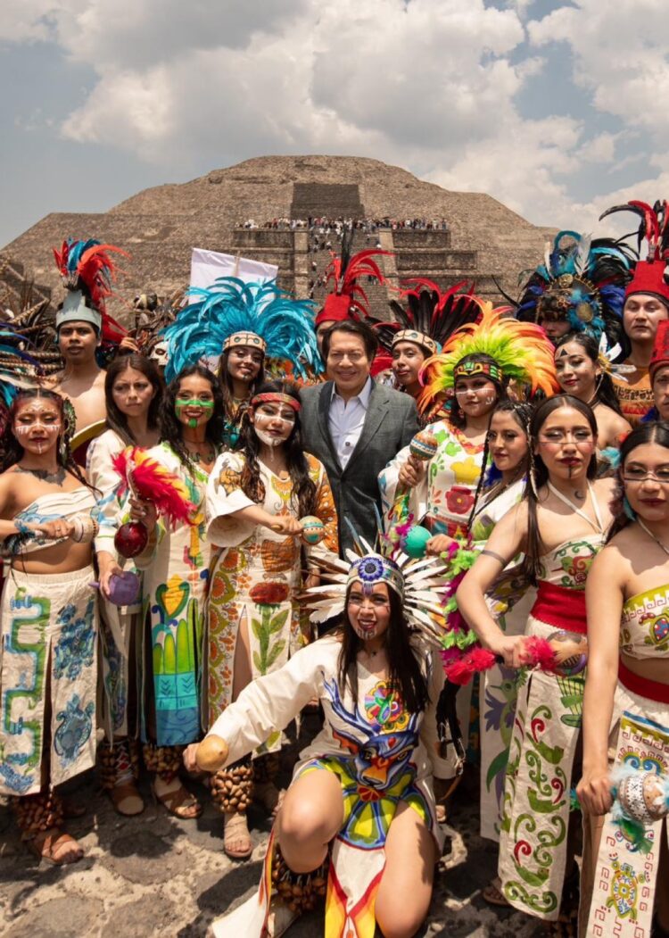 Grupo de personas con trajes tradicionales y plumas en Teotihuacán, celebrando el encendido del Fuego Nuevo rumbo a Juegos Ce.