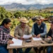 Grupo de agricultores y técnicos discuten en campo agrícola con tractor en fondo.