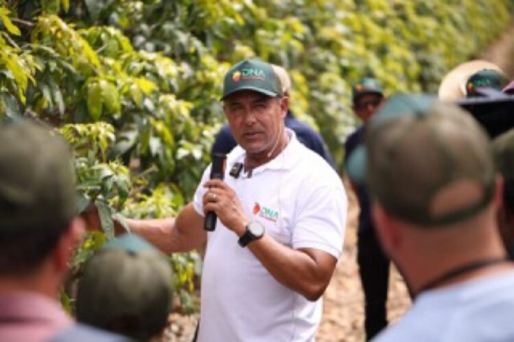 Hombre hablando con grupo de agricultores en un campo de cultivo, usando gorra y camiseta blanca, en un entorno agrícola.