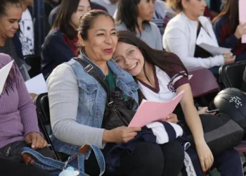 Dos mujeres sonrientes en un evento escolar, compartiendo un momento de alegría y camaradería entre estudiantes y docentes en.