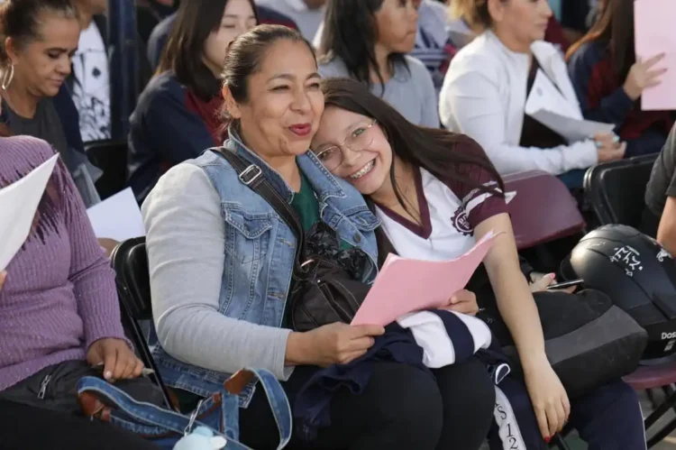 Dos mujeres sonrientes en un evento escolar, compartiendo un momento de alegría y camaradería entre estudiantes y docentes en.
