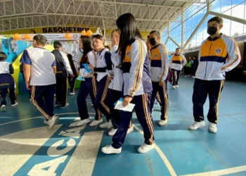 Estudiantes con uniformes deportivos en un espacio cerrado, participando en actividades relacionadas con el baloncesto.