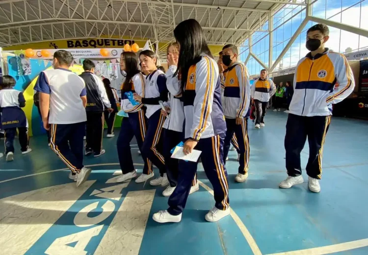 Estudiantes con uniformes deportivos en un espacio cerrado, participando en actividades relacionadas con el baloncesto.