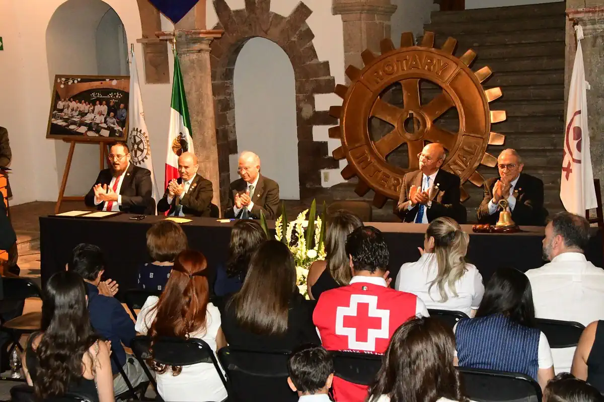 Participantes en una conferencia del Rotary en un espacio con decoraciones tradicionales y un gran engranaje de madera en el.