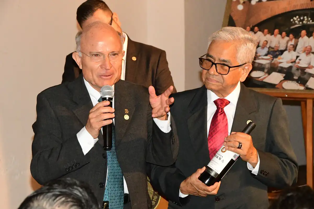 Hombres de negocios en evento formal, uno con micrófono y otro con botella de vino, en una reunión oficial en Michoacán.