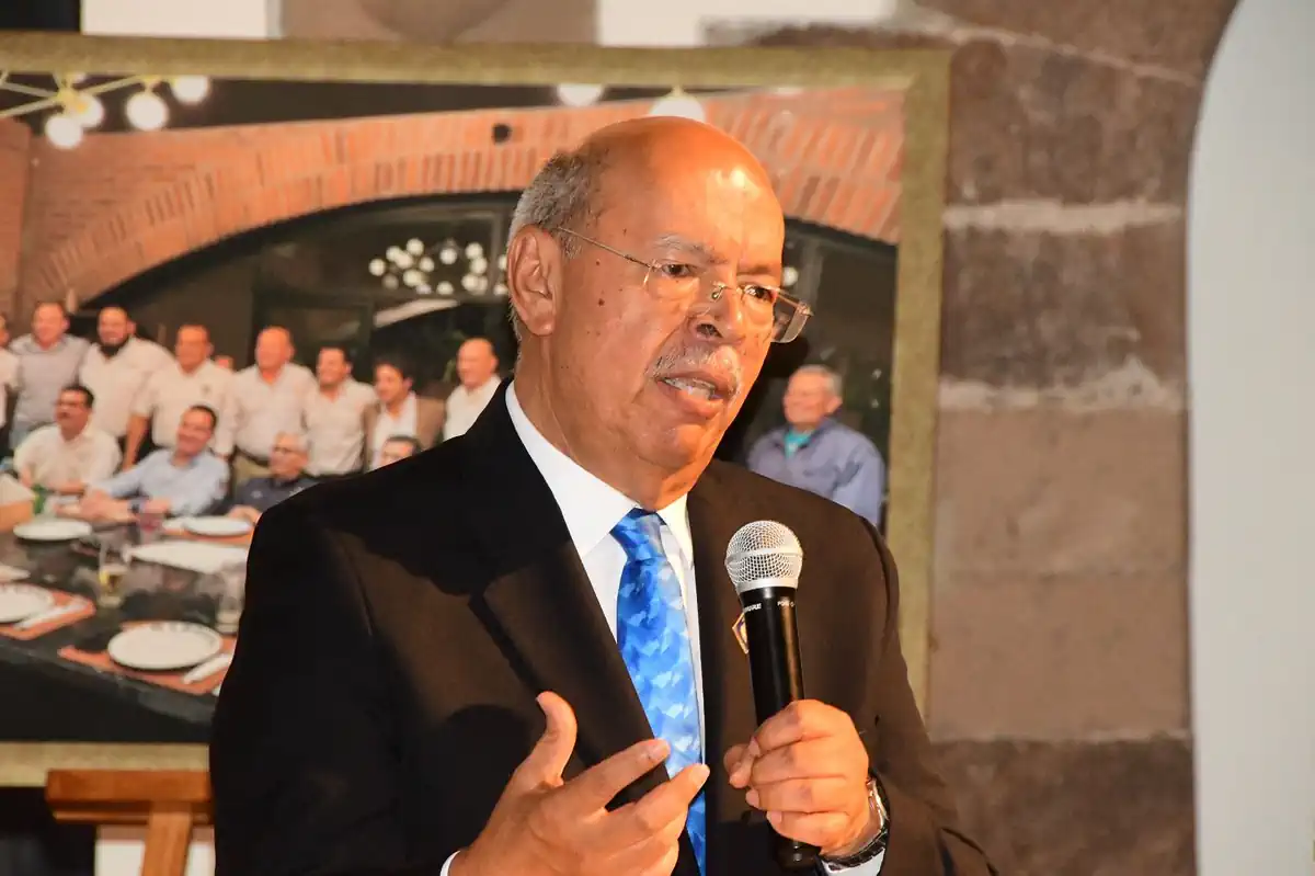 Hombre mayor con gafas y traje negro hablando con micrófono en evento político en Michoacán.