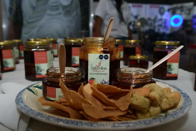 Mermeladas de mango en frascos pequeños acompañadas de galletas y papeles de seda en una bandeja.