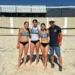Jóvenes atletas femeninas en uniforme de voleibol en la arena junto a su entrenador en la playa.