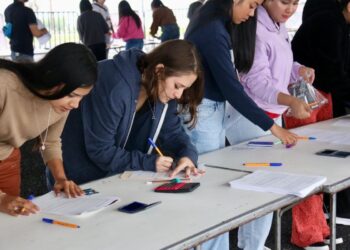 Estudiantes revisan documentos y llenan formularios en una mesa durante proceso de inscripción.