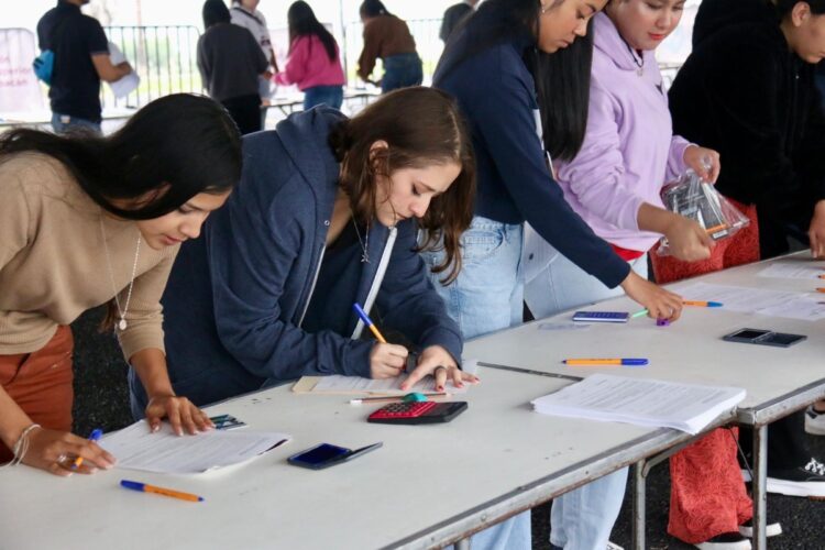 Estudiantes revisan documentos y llenan formularios en una mesa durante proceso de inscripción.