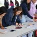 Estudiantes revisan documentos y llenan formularios en una mesa durante proceso de inscripción.