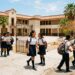 Amplia vista de estudiantes en uniforme escolar en patio de escuela con edificios y palmeras en fondo.