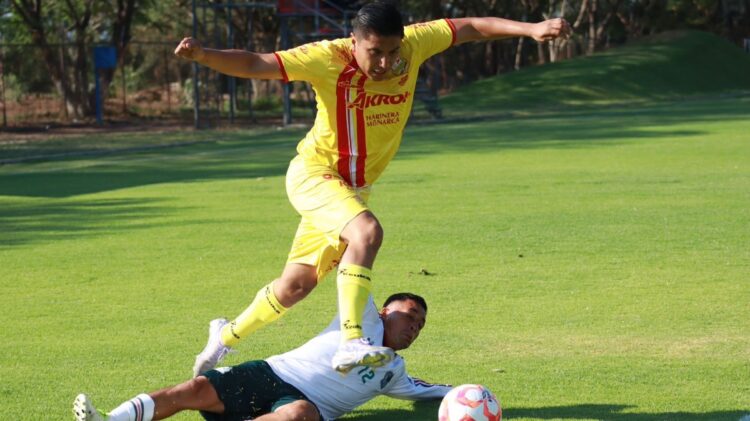 Jugador en uniforme amarillo saltando sobre oponente en campo de fútbol durante partido en exteriores.