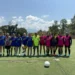 Jugadoras de fútbol femenino en entrenamiento en un campo al aire libre con árboles y cielo despejado de fondo.