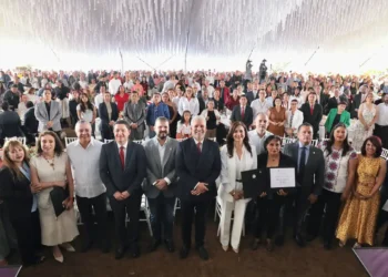Personas en evento formal con reconocimiento y certificado en un espacio decorado con techumbre blanca.