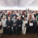 Personas en evento formal con reconocimiento y certificado en un espacio decorado con techumbre blanca.