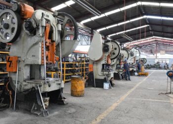 Maquinarias industriales en una planta de producción con maquinaria pesada y operarios trabajando en un ambiente industrial.