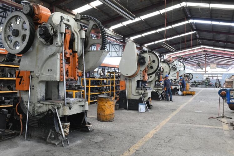 Maquinarias industriales en una planta de producción con maquinaria pesada y operarios trabajando en un ambiente industrial.