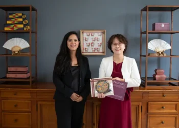 Mujeres sosteniendo un libro y un certificado en un entorno de oficina elegante.