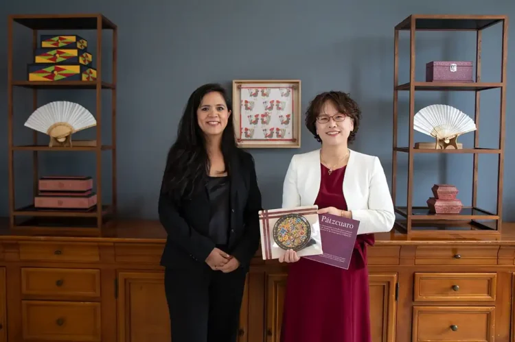 Mujeres sosteniendo un libro y un certificado en un entorno de oficina elegante.