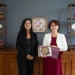 Mujeres sosteniendo un libro y un certificado en un entorno de oficina elegante.