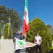 Jóvenes sosteniendo una bandera mexicana y un cartel en un parque con árboles y cielo despejado.