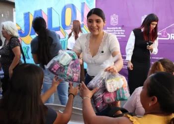 Mujer entrega paquetes a niños en evento cultural en Michoacán.