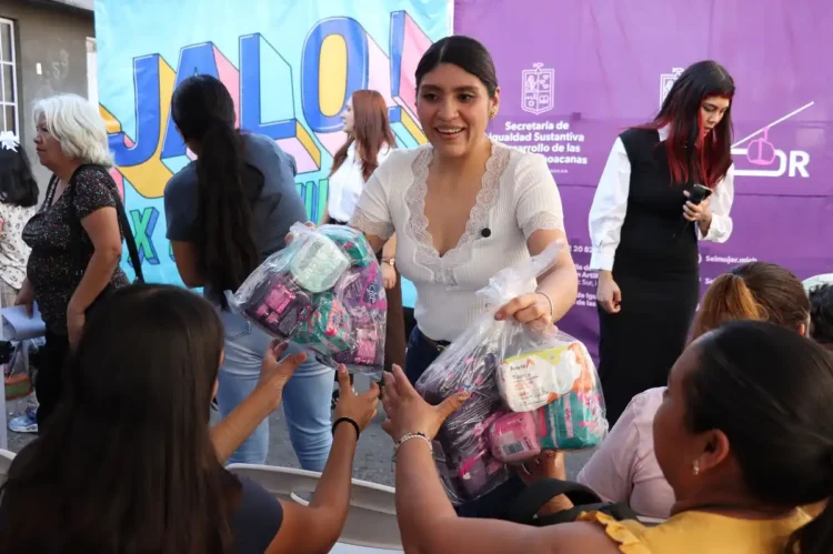 Mujer entrega paquetes a niños en evento cultural en Michoacán.