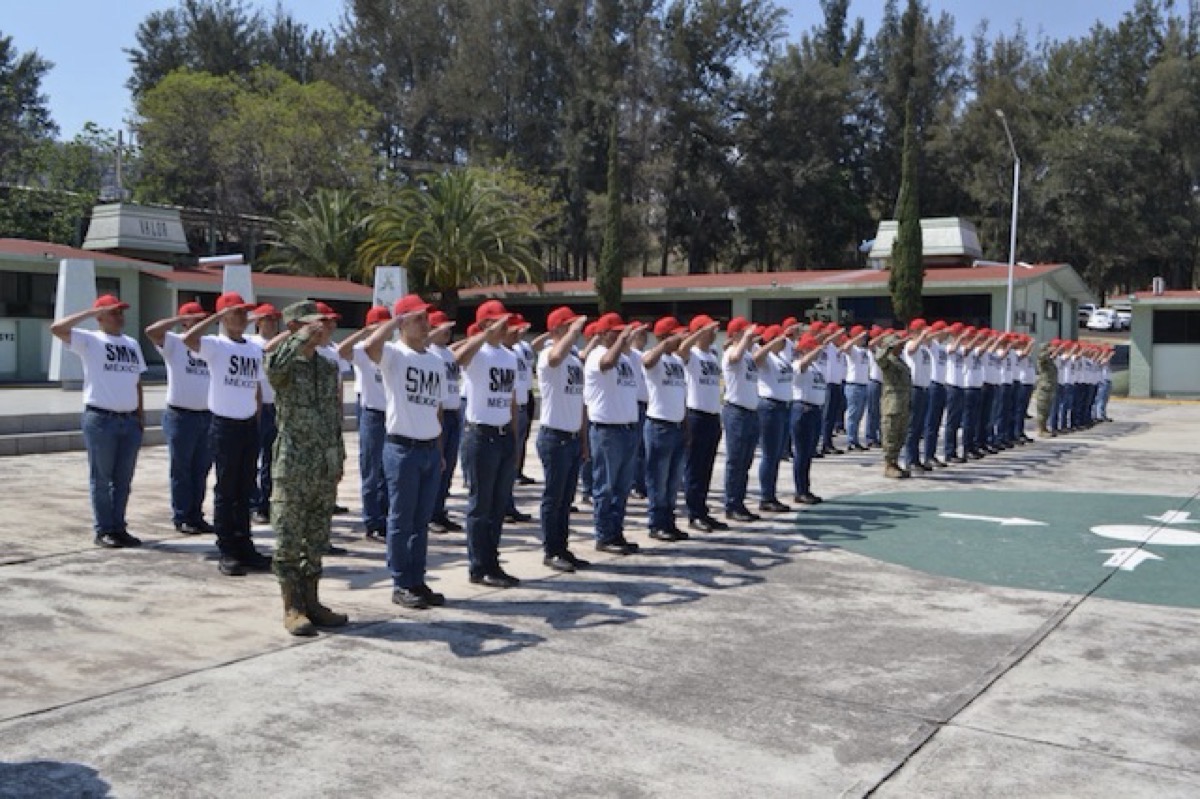 Jóvenes en formación militar durante ceremonia en Zamora, Michoacán, con uniformes y sombreros rojos, en un acto de graduació.