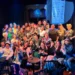Grupo de personas en el escenario de El Breve, participando en un evento con risas y alegría.