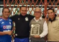 Cuatro personas posan con un reconocimiento en un evento formal en Michoacán, con fondo de madera y ambiente de celebración.