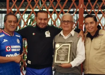 Cuatro personas posan con un reconocimiento en un evento formal en Michoacán, con fondo de madera y ambiente de celebración.