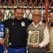 Cuatro personas posan con un reconocimiento en un evento formal en Michoacán, con fondo de madera y ambiente de celebración.