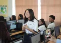 Joven estudiante en aula de computación en Michoacán, participando en clase con sus compañeros en un entorno escolar moder.
