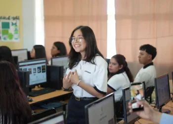 Joven estudiante en aula de computación en Michoacán, participando en clase con sus compañeros en un entorno escolar moder.