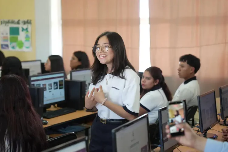 Joven estudiante en aula de computación en Michoacán, participando en clase con sus compañeros en un entorno escolar moder.