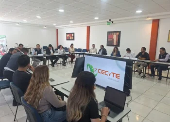 Grupo de personas en reunión en una sala moderna con pantallas y laptops, discutiendo temas educativos en Michoacán.