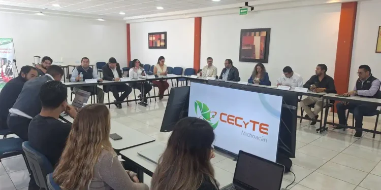 Grupo de personas en reunión en una sala moderna con pantallas y laptops, discutiendo temas educativos en Michoacán.