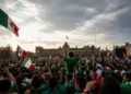 Multitud de personas en una manifestación en la Ciudad de México, ondeando banderas mexicanas bajo un cielo nublado.