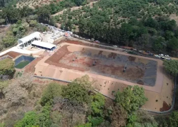 Cancha deportiva en construcción en Michoacán, rodeada de árboles y naturaleza, con maquinaria y materiales en el sitio.