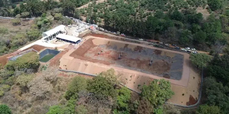 Cancha deportiva en construcción en Michoacán, rodeada de árboles y naturaleza, con maquinaria y materiales en el sitio.