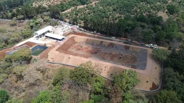 Cancha deportiva en construcción en Michoacán, rodeada de árboles y naturaleza, con maquinaria y materiales en el sitio.