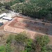 Cancha deportiva en construcción en Michoacán, rodeada de árboles y naturaleza, con maquinaria y materiales en el sitio.
