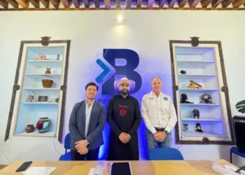 Tres hombres en una sala con estanterías llenas de objetos decorativos y un logo grande en la pared.