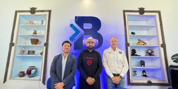 Tres hombres en una sala con estanterías llenas de objetos decorativos y un logo grande en la pared.