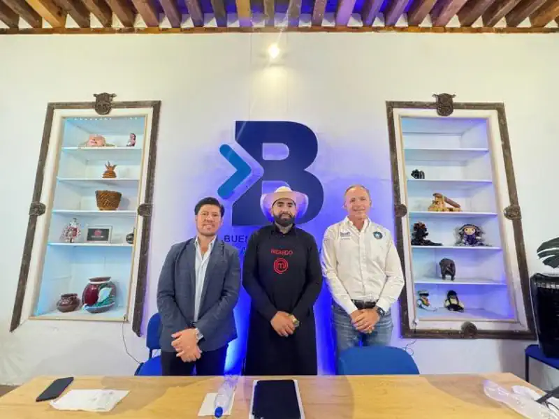 Tres hombres en una sala con estanterías llenas de objetos decorativos y un logo grande en la pared.