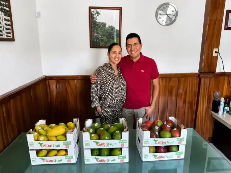 Pareja sonriendo con cajas de frutas en un establecimiento.
