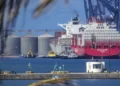 Grúa portuaria y buque de carga en el puerto de Manzanillo, Michoacán, con silos y barcos en el fondo.